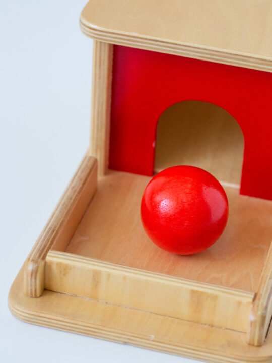 image of Montessori object permanence box and red ball, one of the best enveloping schema toys.