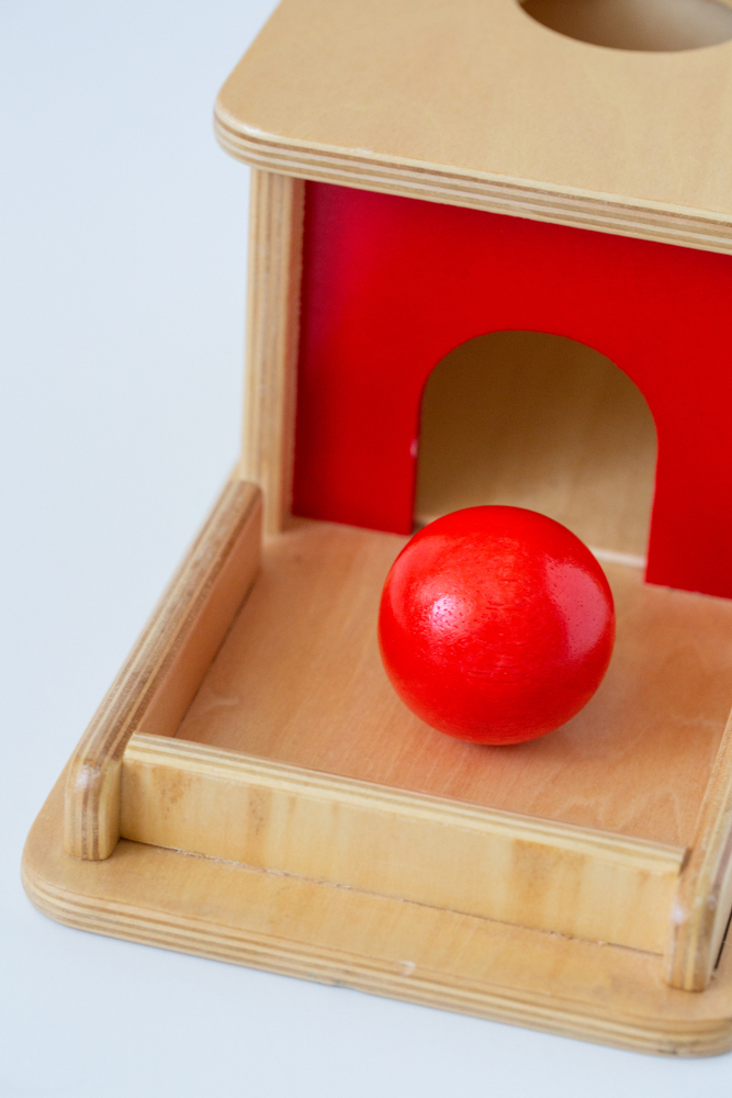 image of Montessori object permanence box and red ball, one of the best enveloping schema toys.