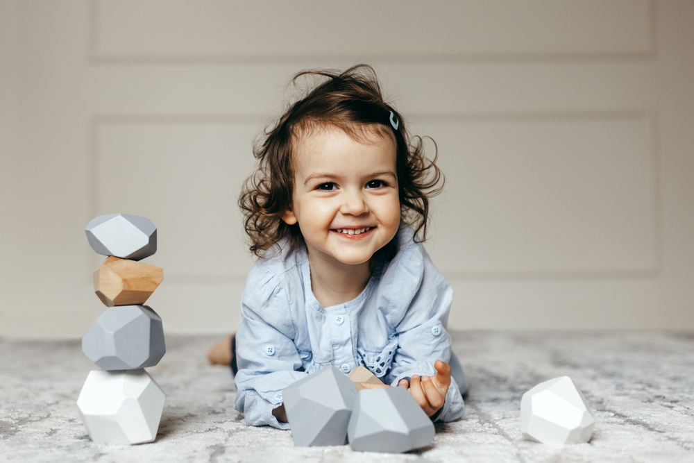 Image of smiling child playing with neutral color Montessori balancing stones.