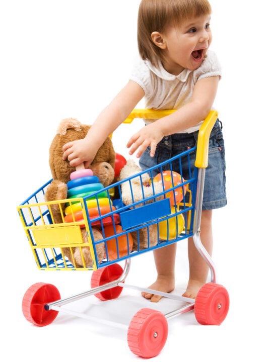image of a young child putting toys in a shopping cart, which shopping carts are transportation schema toys.