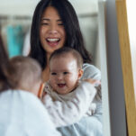 Image of baby looking in the mirror and smiling with smiling mother using Montessori pull up bar.