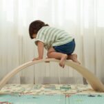 image of toddler climbing on Montessori climbing toys, a wobble board.